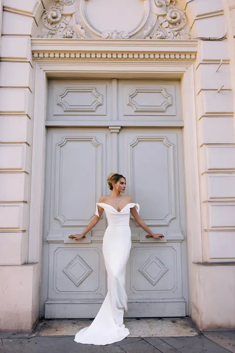 Bride in off-shoulder fitted gown posing in front of a grand carved doorway