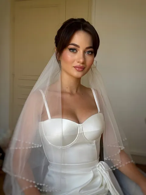 Mariée au voile de tulle bordé de perles, chignon souple avec frange rideau et robe corsetée