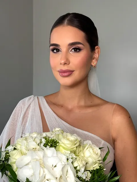 Mariée au chignon lisse et maquillage glamour doux tenant un bouquet de roses blanches