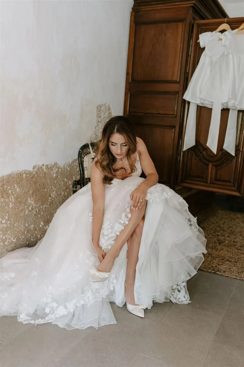 Bride in tulle ball gown adjusting her shoe beside an antique wardrobe