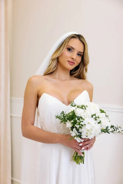 Bride with veil and soft waves in a strapless gown holding a white bouquet