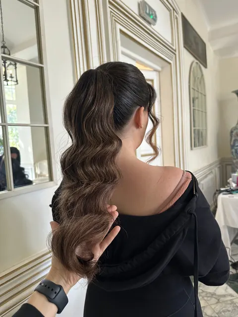 Hairstylist holding a sleek high ponytail with glossy Hollywood waves, back view