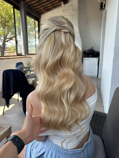 Hairstylist presenting long blonde waves with a twisted half-up detail, back view
