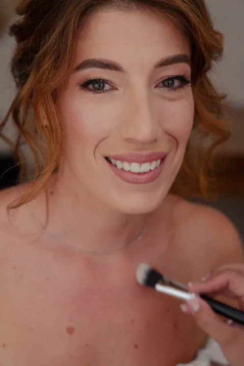 Makeup application in progress: brush on a smiling woman with soft auburn updo