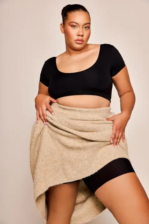 Model in black crop top and beige knit skirt, glowing skin, studio photoshoot look