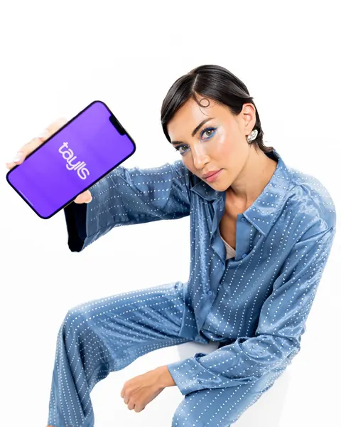 Model in blue pyjamas with graphic eye makeup holding a smartphone, studio