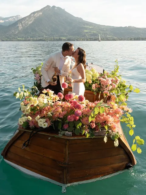 Newlyweds kissing on a flower-covered wooden boat on a mountain lake