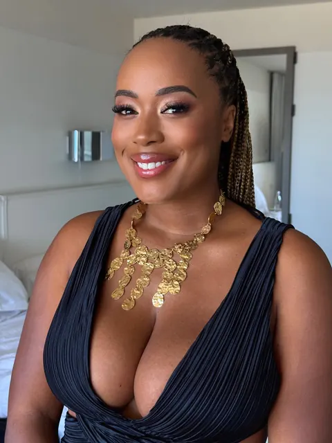Smiling woman with braids, glam makeup and gold statement necklace in a black dress