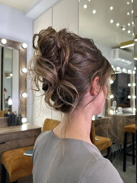 Textured messy updo seen from behind in a makeup studio with lit mirrors