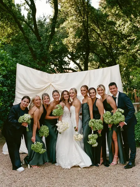 Wedding party in a garden: bride, bridesmaids in green satin and groomsmen, wider frame