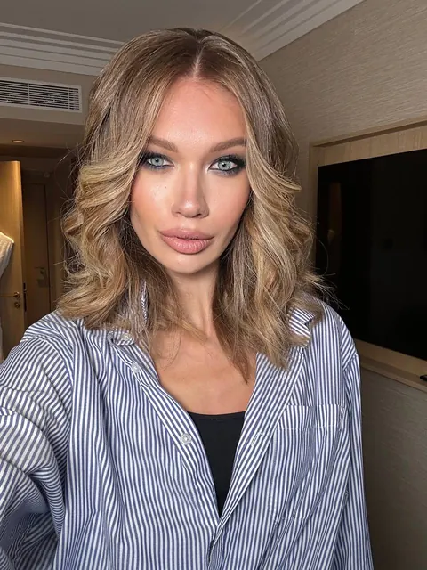 Woman with bouncy shoulder-length waves and smoky eyes in a striped shirt