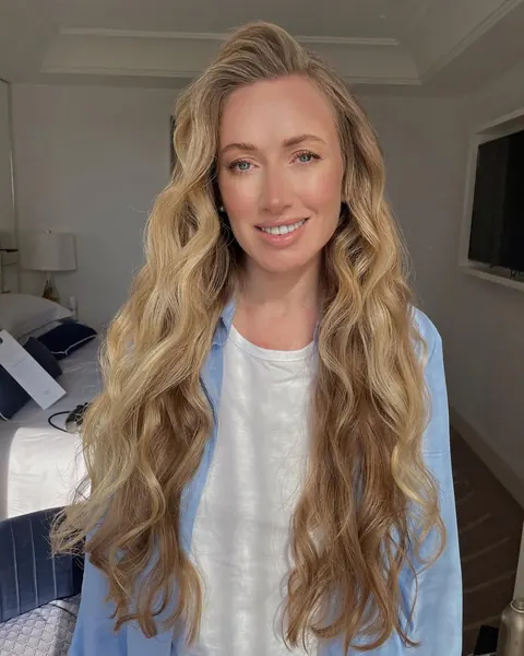 Femme aux longues ondulations blondes façon plage et maquillage naturel dans une chambre d’hôtel