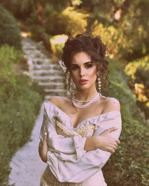 Woman in off-shoulder satin blouse with curly updo and pearls on garden steps