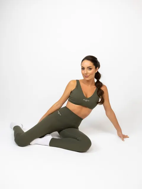 Woman in olive sportswear with braided ponytail sitting on a white studio floor
