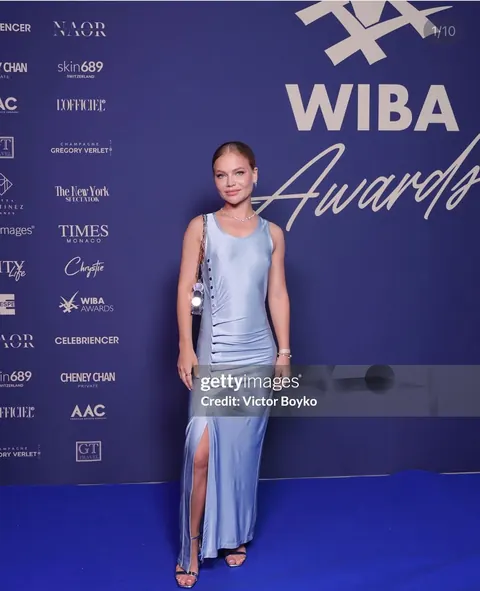 Woman in pale blue satin dress at an awards event backdrop