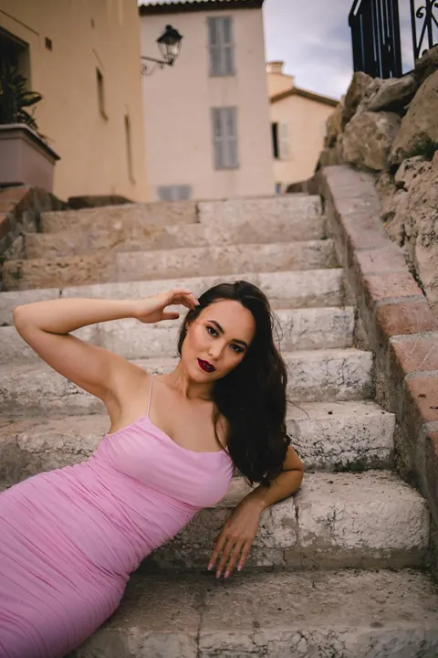 Woman in pink bodycon dress reclining on old stone steps, dark lipstick