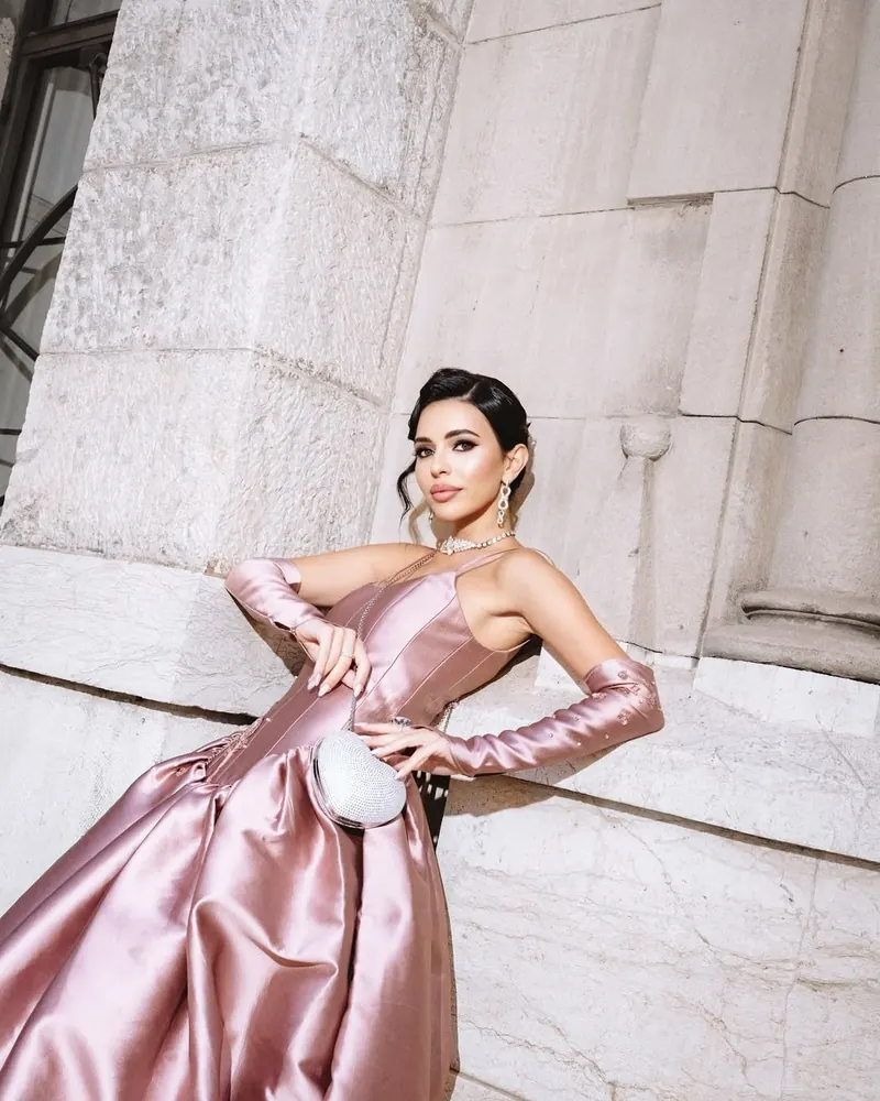 Femme en robe de satin rose et longs gants posant contre un mur de pierre