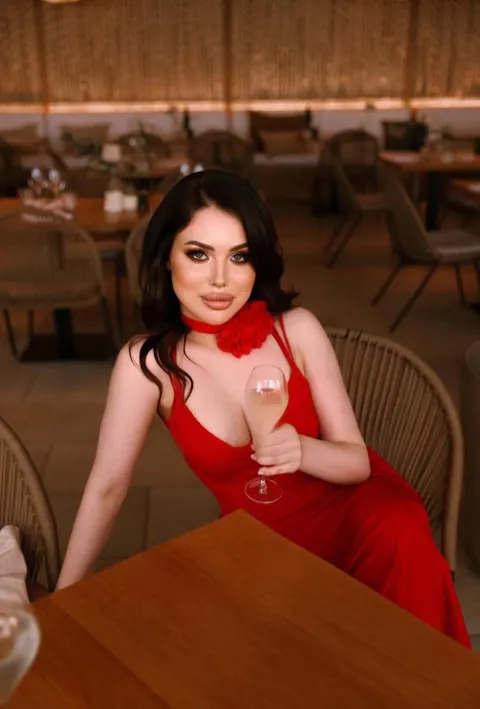 Woman in red dress with rose choker holding a wine glass at a restaurant table