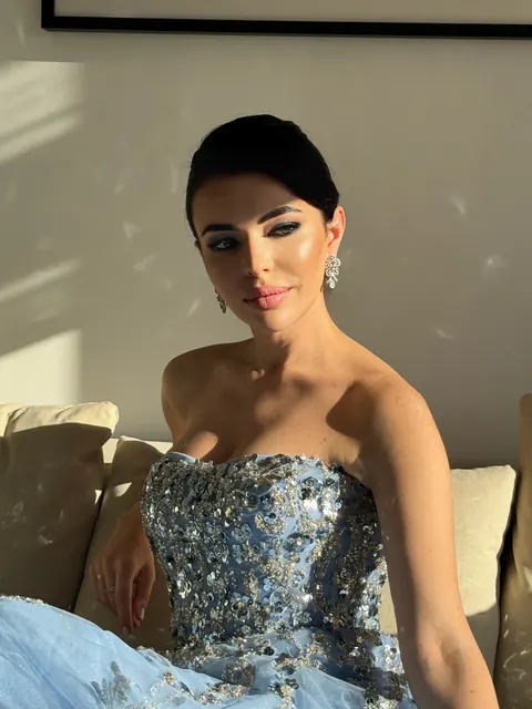 Woman in sequined strapless blue gown with sleek bun and winged liner in sunlight
