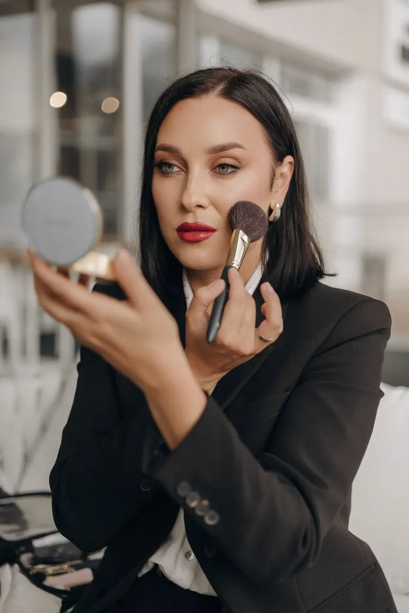 Woman with sleek bob applying blush with a brush and compact mirror