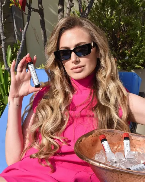 Woman in sunglasses and pink dress holding a beauty shot by an ice bowl, close crop