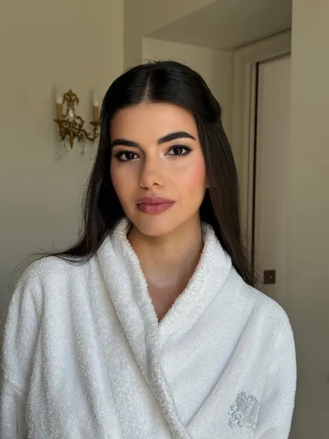 Woman in white bathrobe with long sleek hair and soft bridal makeup, getting ready