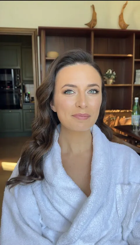 Woman in white bathrobe with soft side-swept waves and natural glam makeup