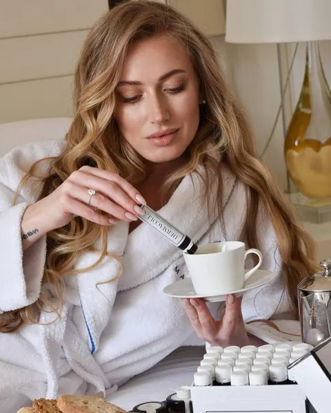 Woman in white robe with long waves pouring a beauty shot into a teacup