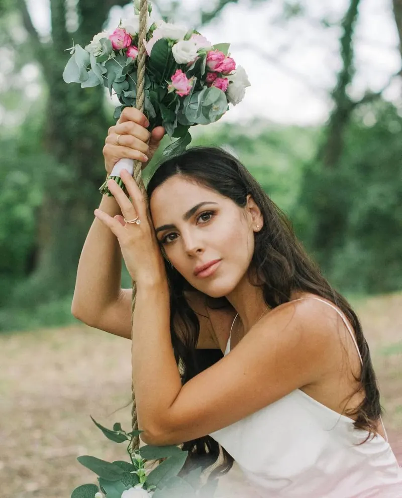 Femme en robe nuisette blanche tenant une balançoire décorée de roses en plein air